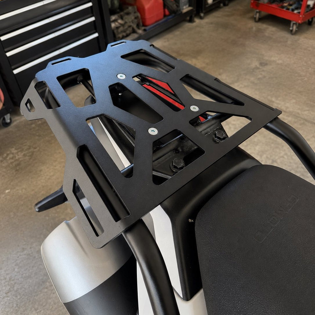 A black metal luggage rack mounted on the back of a CFMOTO 250DUAL in a workshop setting.